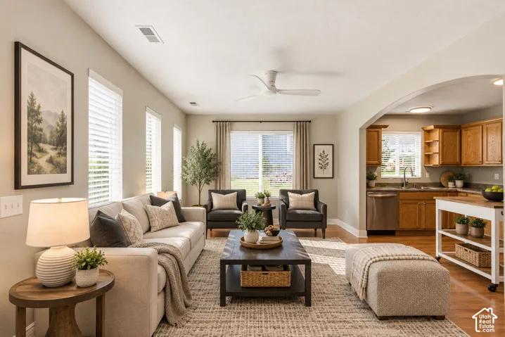 Open-concept living space featuring vaulted ceilings, wood-finish flooring, a white ceiling fan, and a wide arched entryway leading to the kitchen cabinetry
