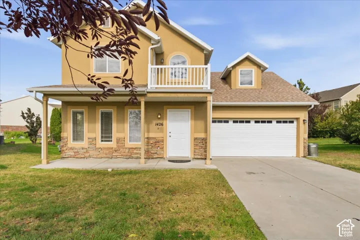 Two-story exterior featuring a stucco facade with stone veneer accents, an upper-level railed balcony, a covered porch, and an attached two-car garage