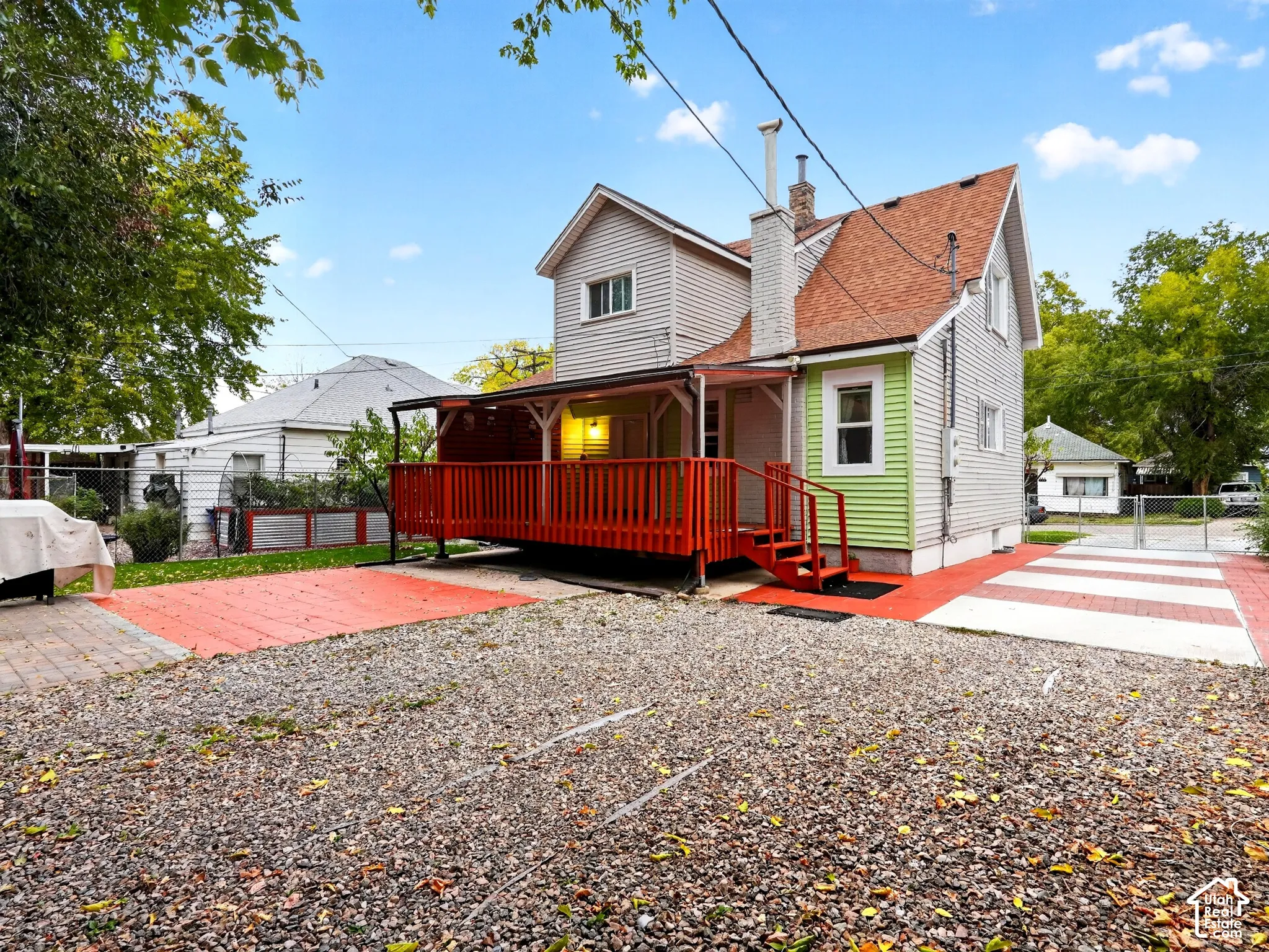 Exterior view featuring multi-level lap siding, a raised covered deck with railing, a brick chimney, and a multi-surface paved area