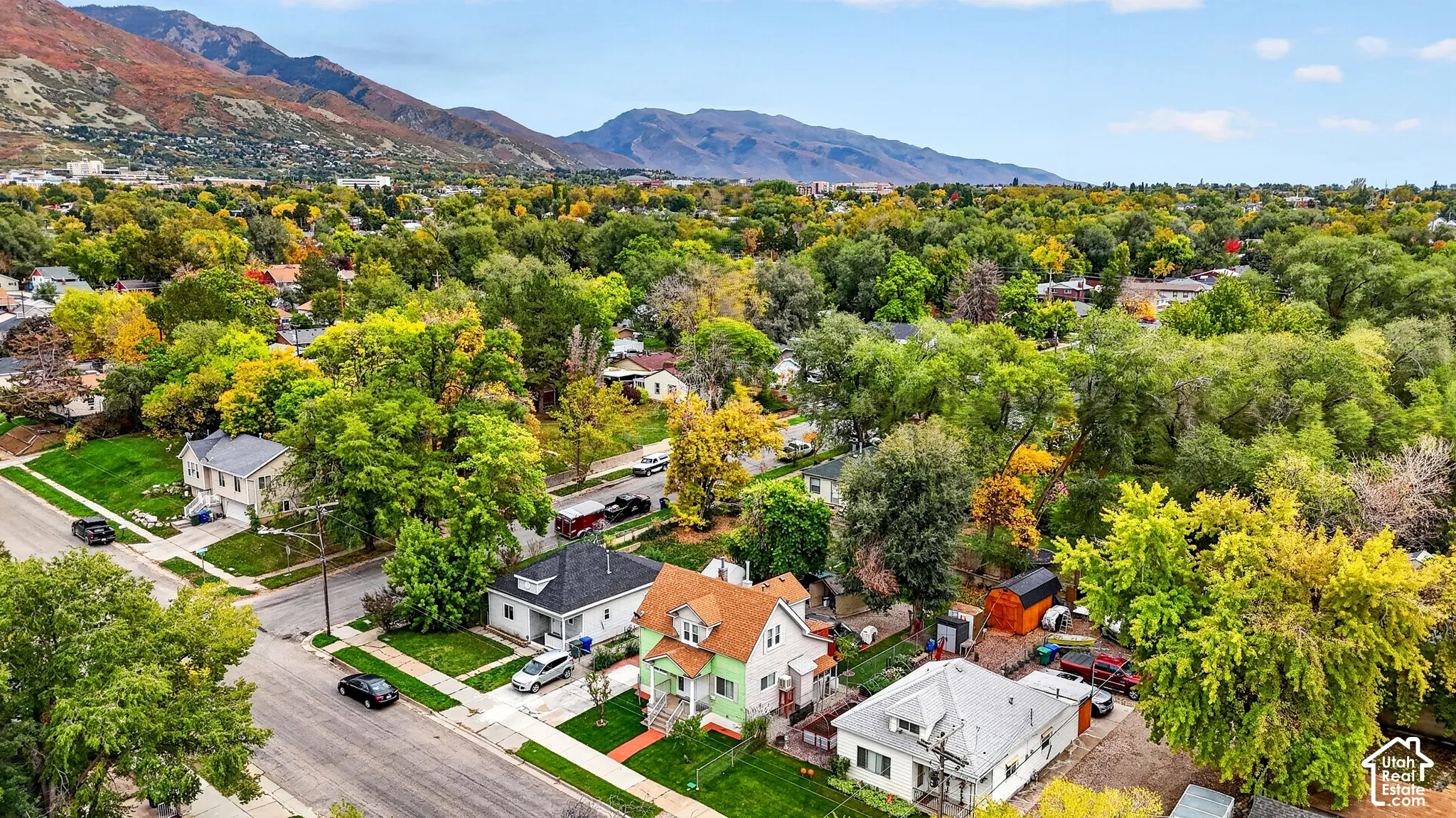 Aerial perspective featuring a multi-story residence with a pitched shingle roof, mature trees, and mountainous terrain in the background