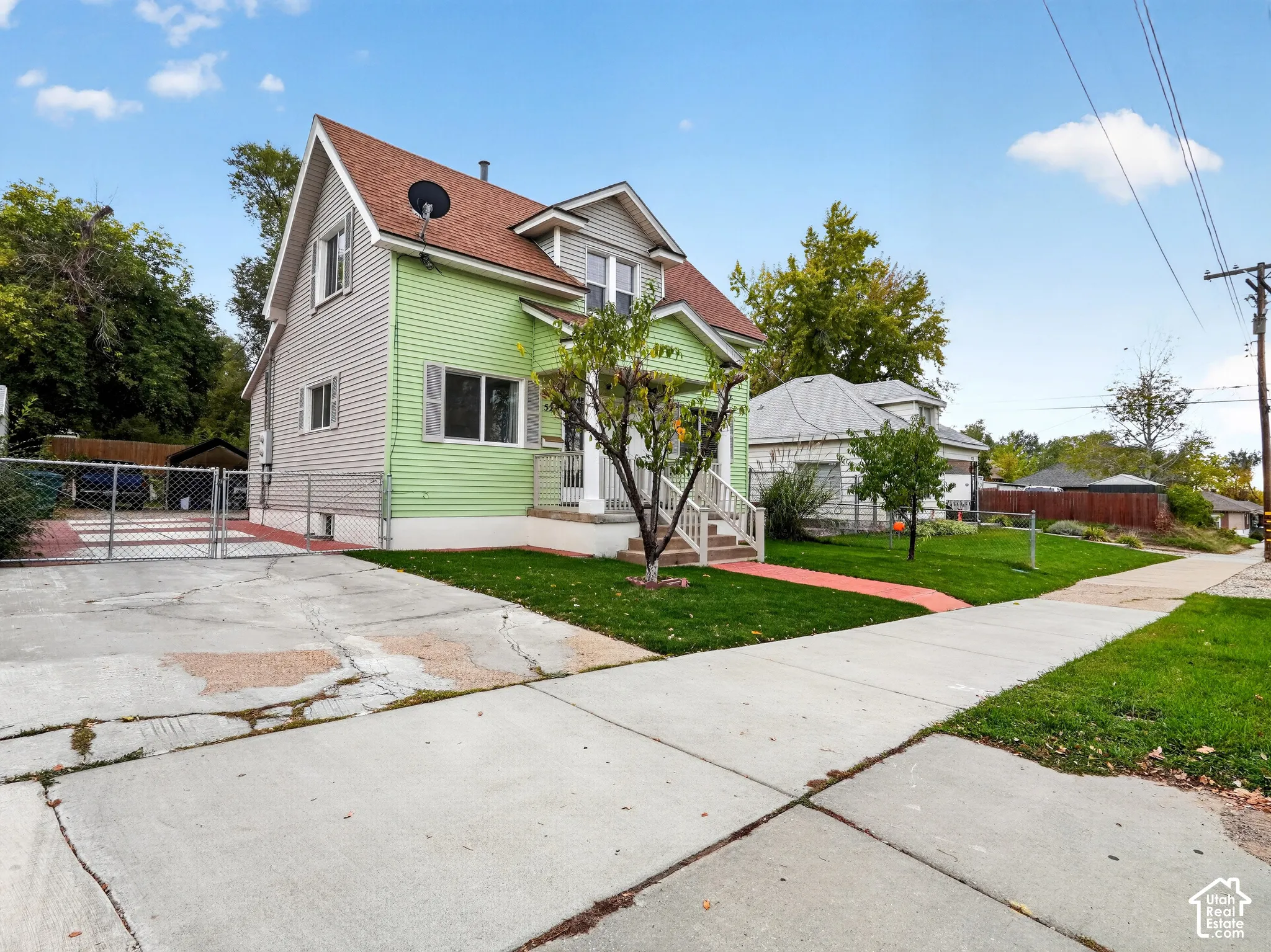 Two-story home with horizontal siding, pitched roof, covered front porch with railings, and concrete driveway with metal perimeter fencing
