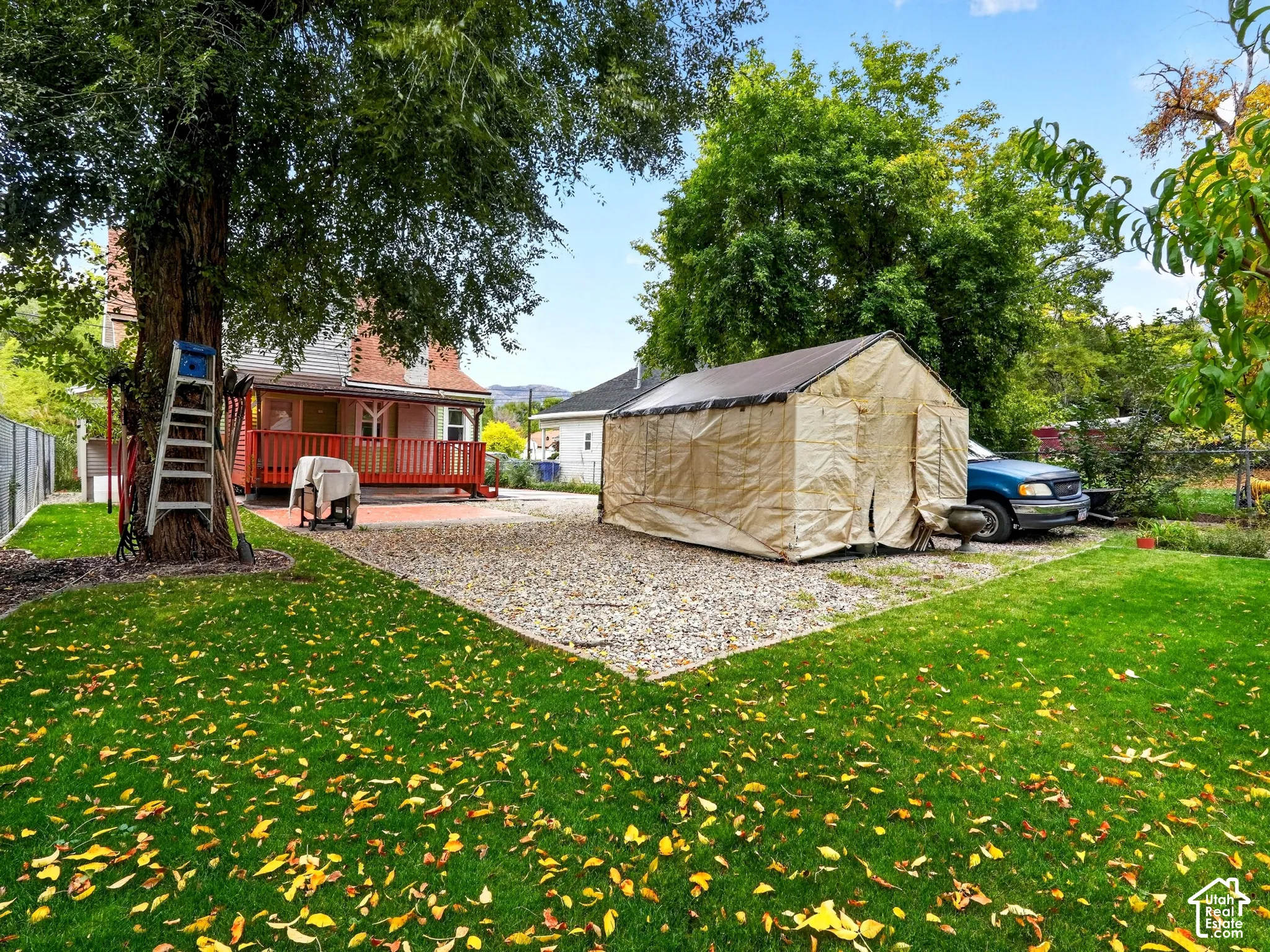 Backyard space featuring a grass lawn, gravel ground cover, a raised deck with wooden railing, and mature trees