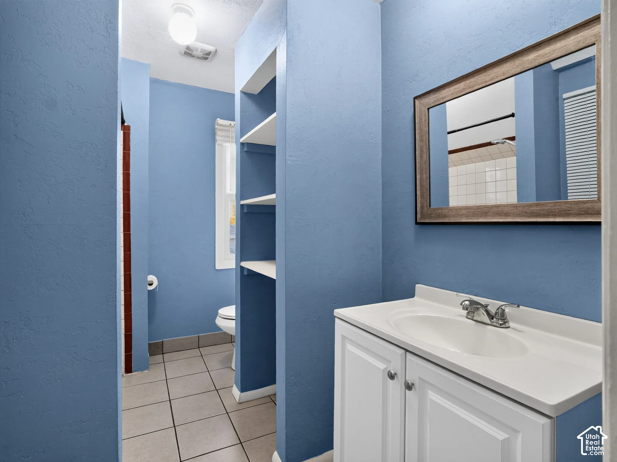 1 bedroom unit - Bathroom featuring a white vanity cabinet with a integrated sink, wood-framed wall mirror, and built-in wall shelving
