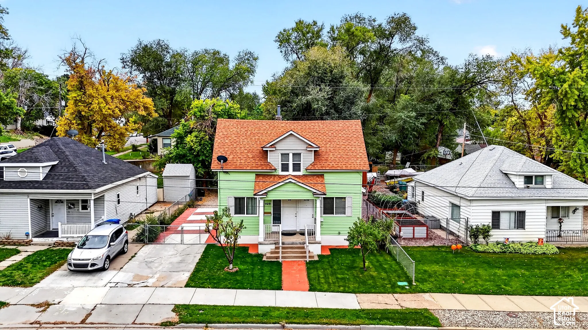 Two-story exterior featuring a gabled roof, front-facing dormer, covered porch with concrete steps, and a fenced yard with mature trees