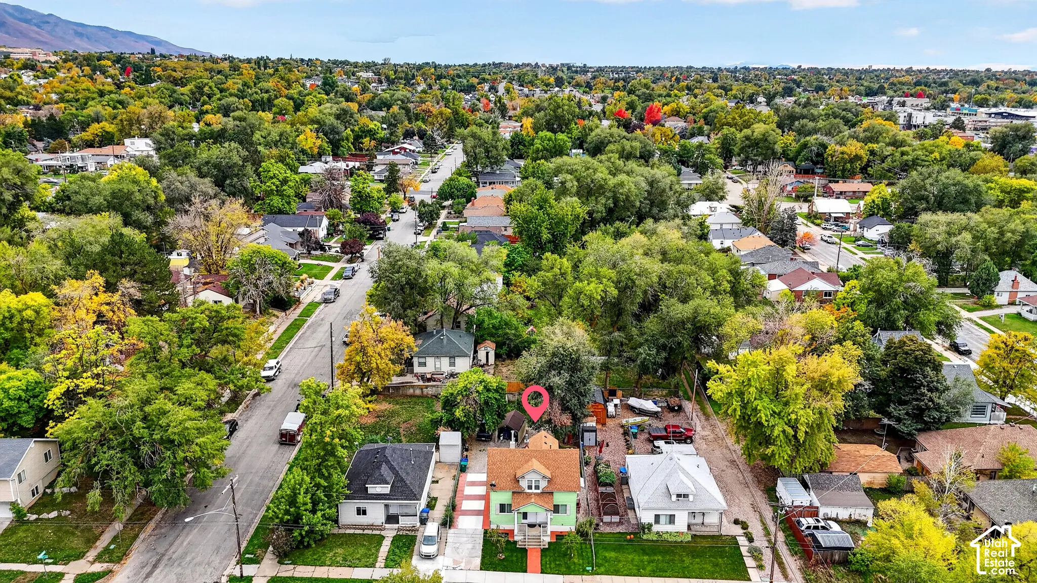 Aerial perspective featuring a multi-story residence with a pitched roof, front porch, paved driveway, and established tree canopy