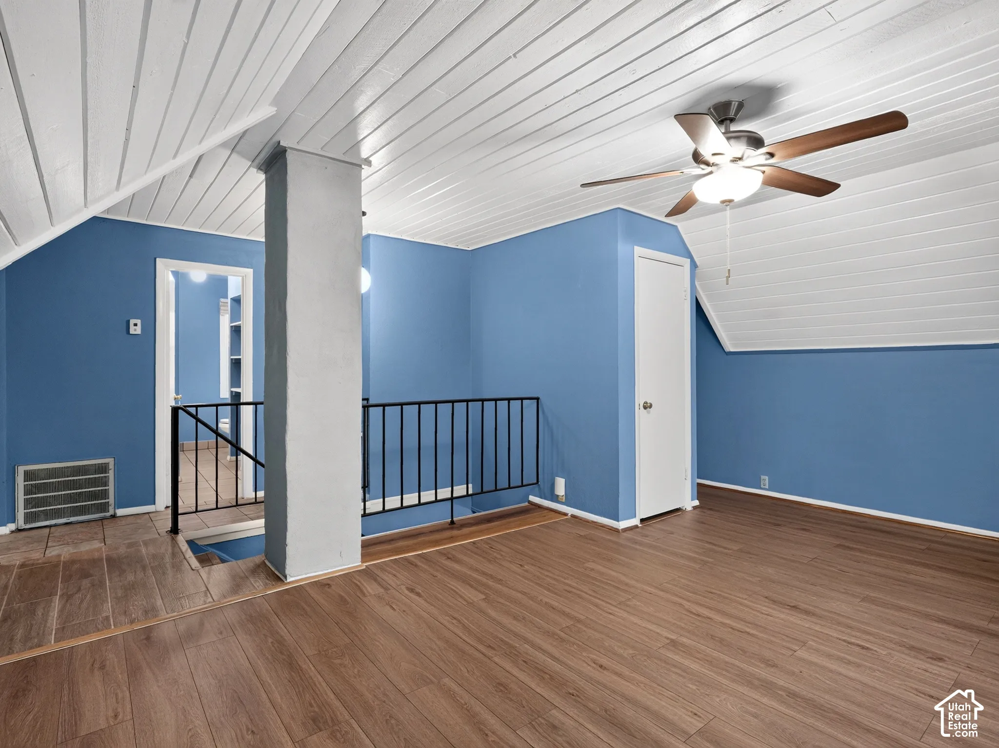 1 bedroom unit - Loft/living room/IVaulted ceiling with tongue-and-groove paneling, wood-finish flooring, metal staircase railing, and ceiling fan with integrated lighting