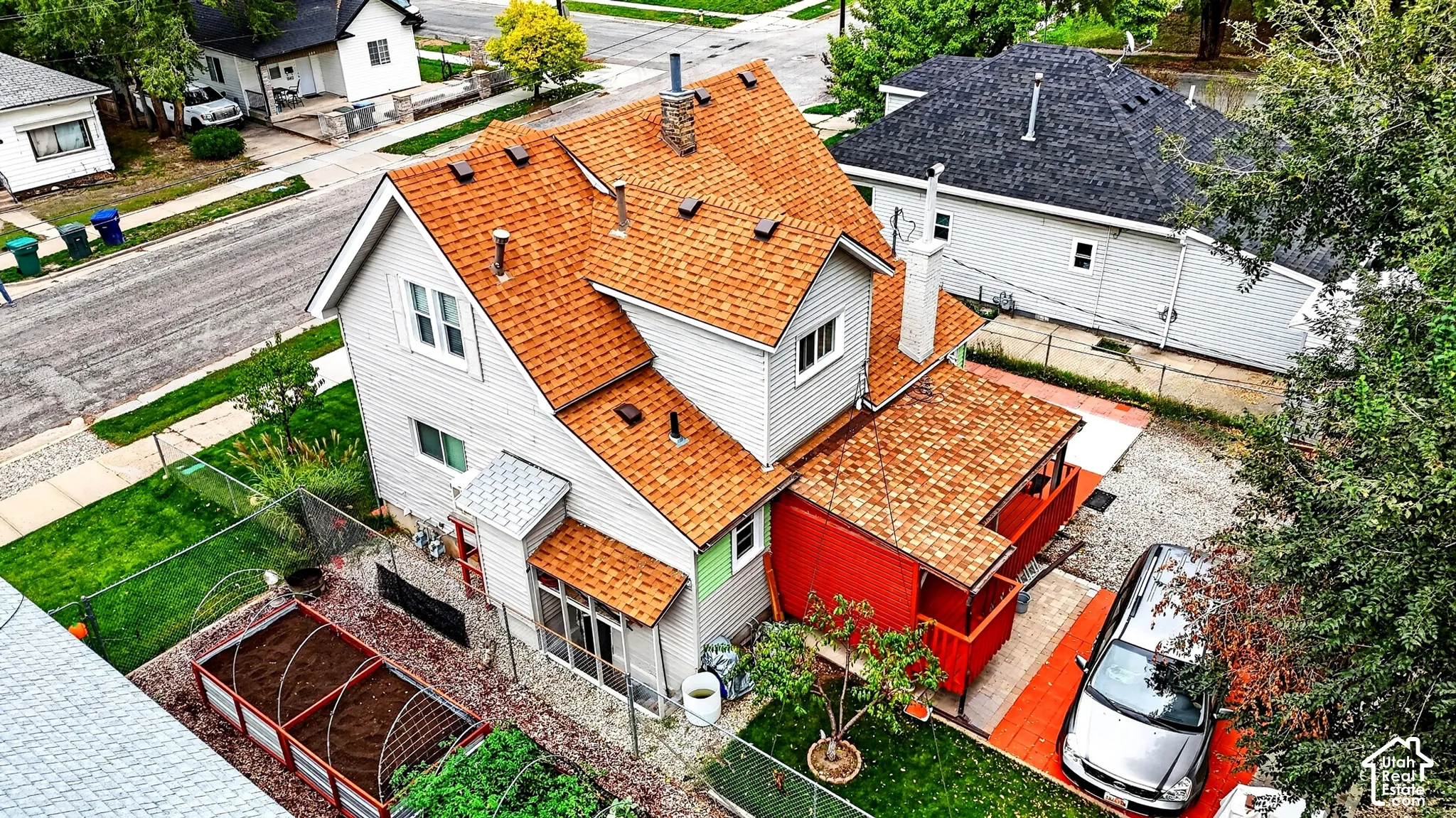 Multi-story residence featuring grey siding, an asphalt shingle roof, a red-accented covered porch, and raised garden beds