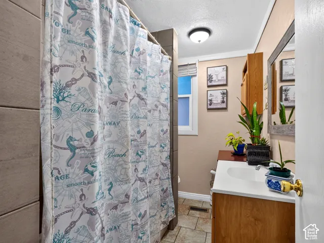 2 bedroom unit - Bathroom featuring a vanity with a white solid-surface countertop, integrated basin, and natural wood-tone cabinetry, tiled shower surround, stone-finish tile flooring, and a framed mirror