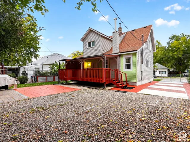 Exterior view featuring multi-level lap siding, a raised covered deck with railing, a brick chimney, and a multi-surface paved area