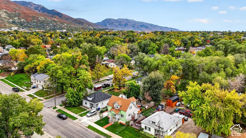 Aerial perspective featuring a multi-story residence with a pitched shingle roof, mature trees, and mountainous terrain in the background