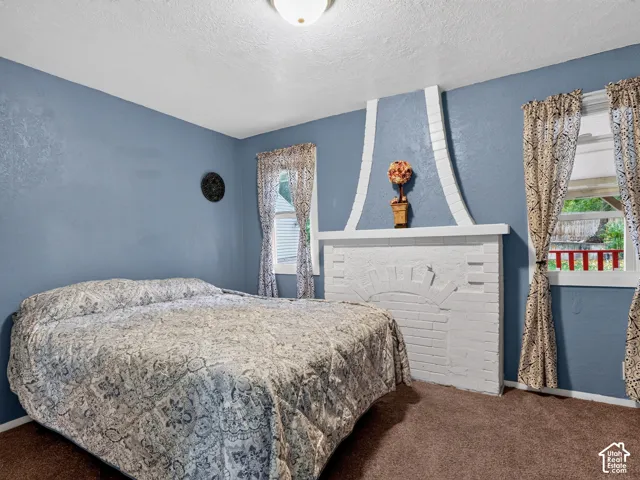 2 bedroom unit - Bedroom 1 featuring a prominent white painted brick fireplace with a decorative arched surround and mantel, brown carpeting, and dual windows