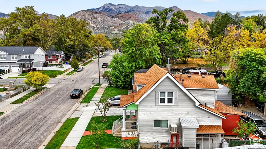 Two-story residence featuring horizontal siding, asphalt shingle roofing, and a front porch with metal railings, positioned against a backdrop of mountain scenery