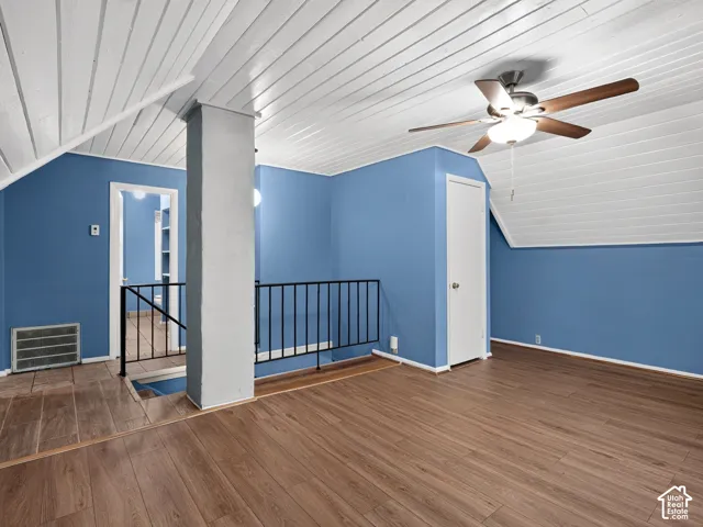 1 bedroom unit - Loft/living room/IVaulted ceiling with tongue-and-groove paneling, wood-finish flooring, metal staircase railing, and ceiling fan with integrated lighting