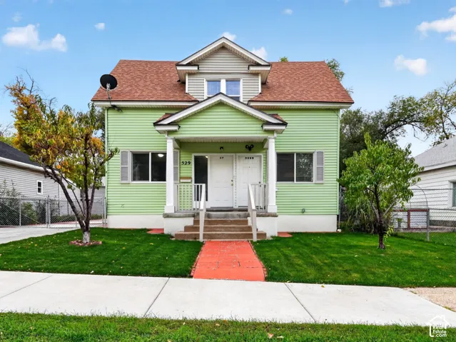 Two-story exterior featuring light green siding, a gabled roofline with dormer, covered front porch with columns, and a concrete walkway