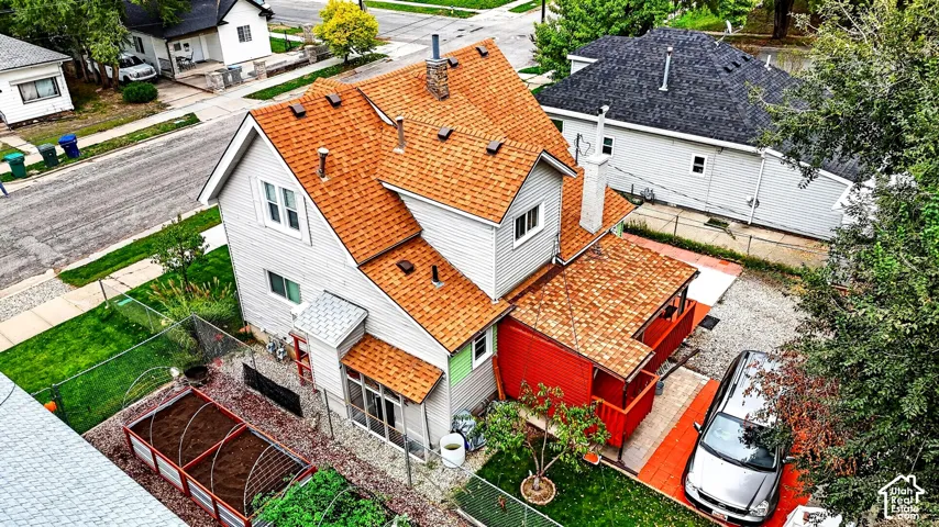 Multi-story residence featuring grey siding, an asphalt shingle roof, a red-accented covered porch, and raised garden beds