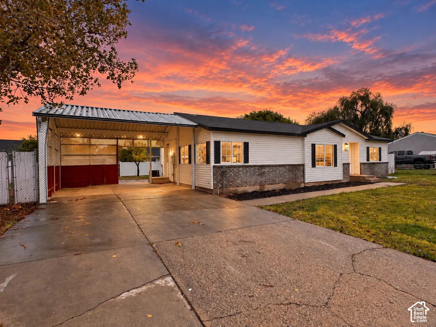 Single-story exterior featuring a metal-roofed carport, stone masonry wainscoting, white horizontal siding, and concrete driveway