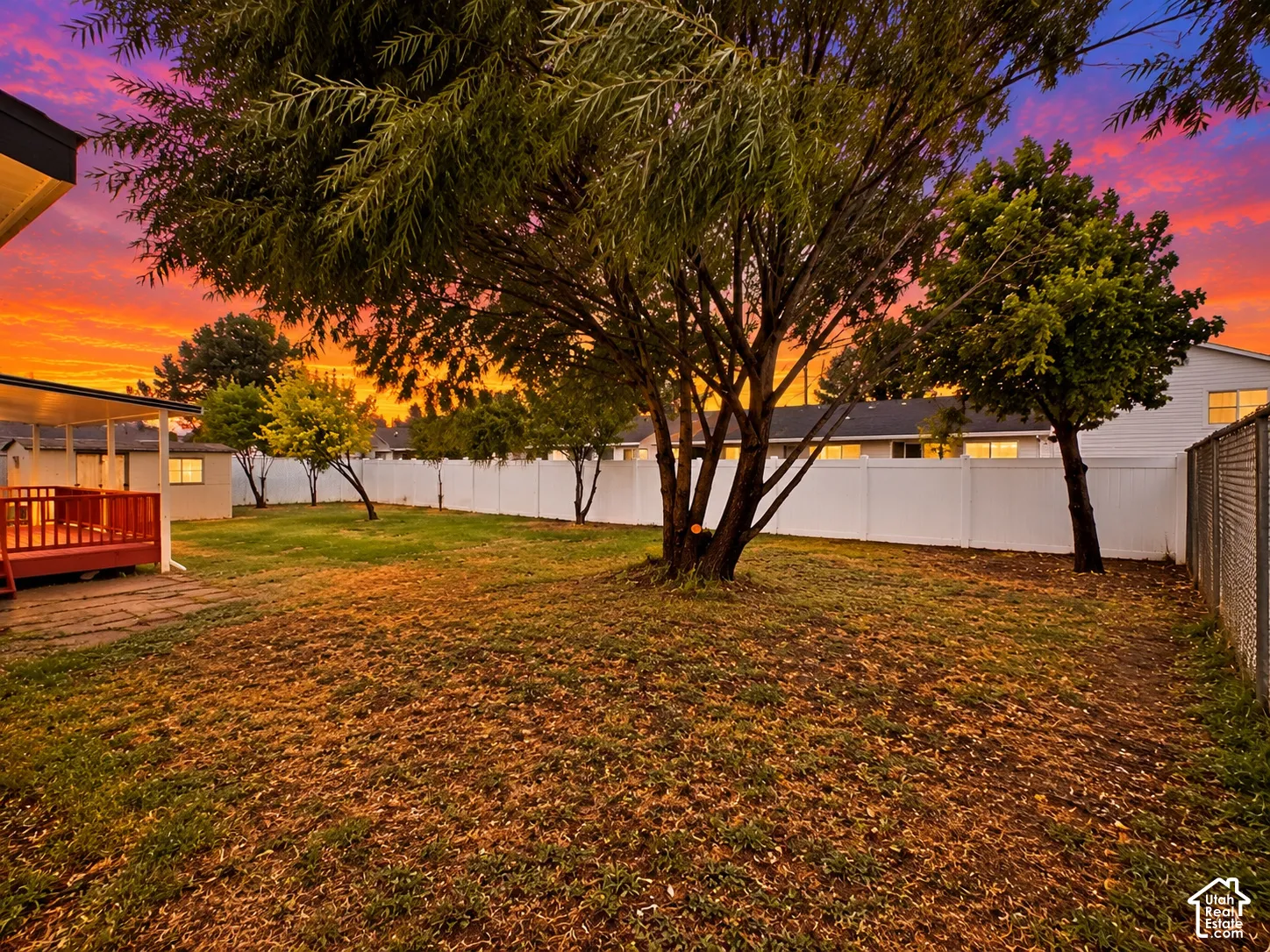 Rear yard featuring a lawn, mature trees, white vinyl privacy fencing, and an attached deck