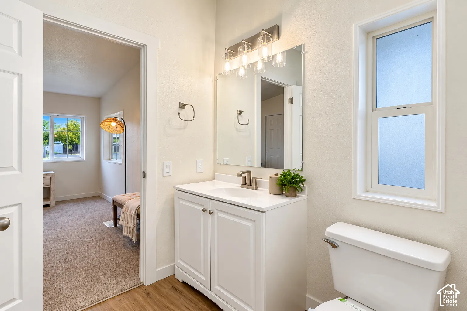 Bathroom featuring a white vanity cabinet with a solid surface countertop, an integrated basin, a three-light fixture, a rectangular wall mirror, and a window with frosted glass