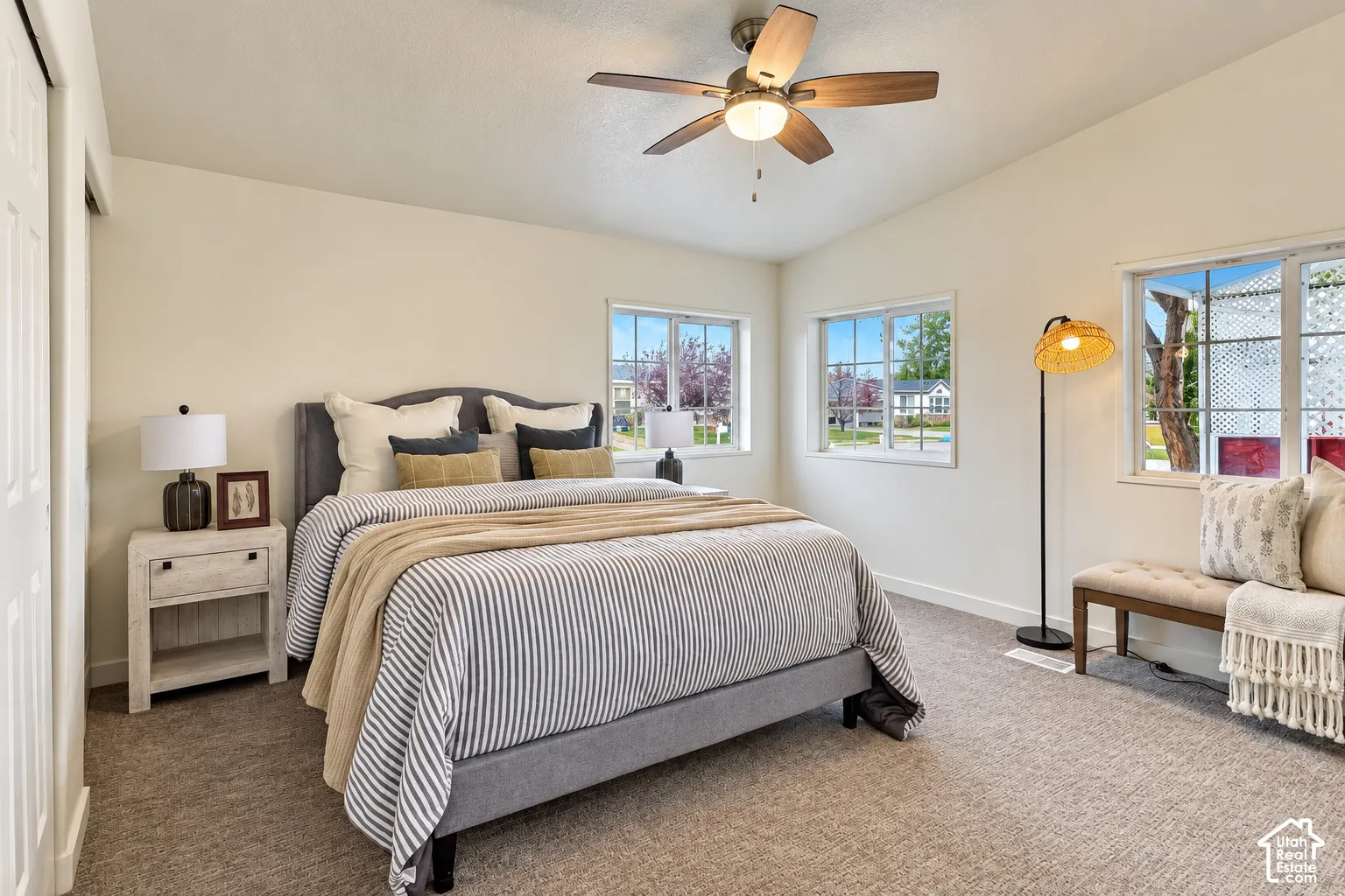 Neutral-toned interior space featuring vaulted ceilings, multi-pane windows, and a ceiling fan with integrated lighting