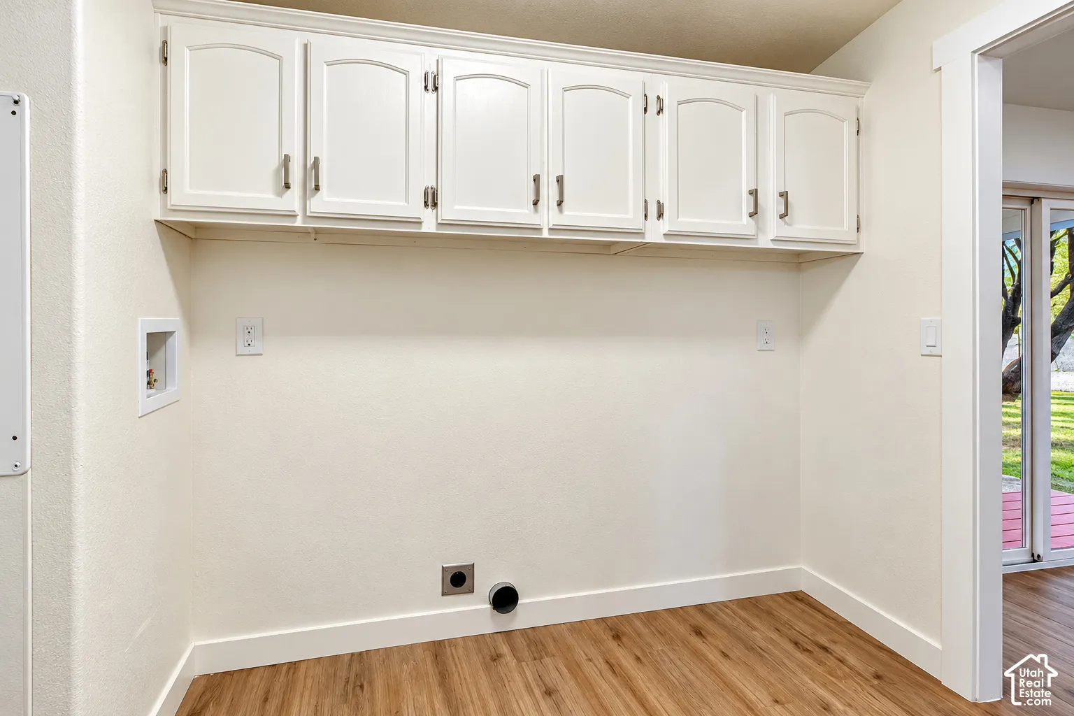 Utility space featuring white shaker-style wall cabinetry, wood-finish flooring, and dedicated laundry hookups