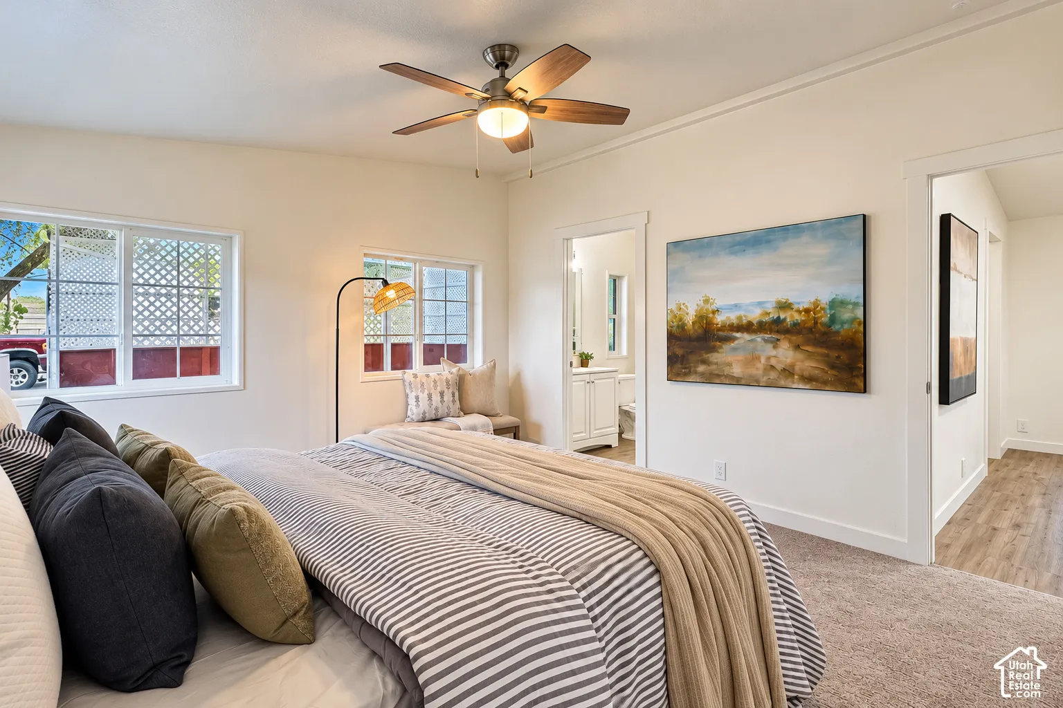Neutral-toned interior featuring wall-to-wall carpeting, multiple grid-patterned windows, ceiling fan with integrated lighting, and wood-finish flooring in the hallway