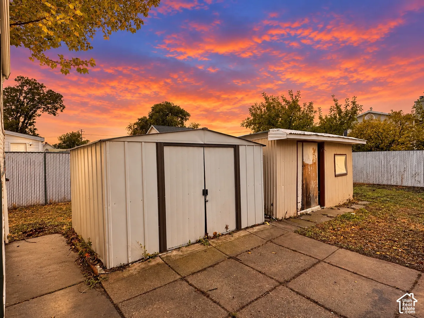 Exterior storage area featuring metal sheds, concrete paving, and perimeter fencing