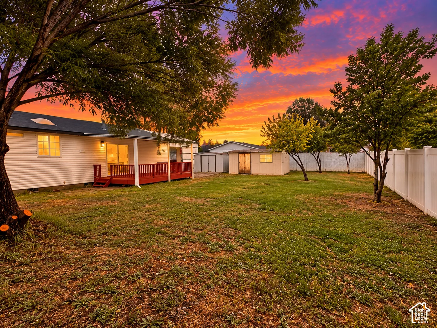 Expansive backyard featuring a wood deck, detached storage structure, privacy fencing, and mature trees