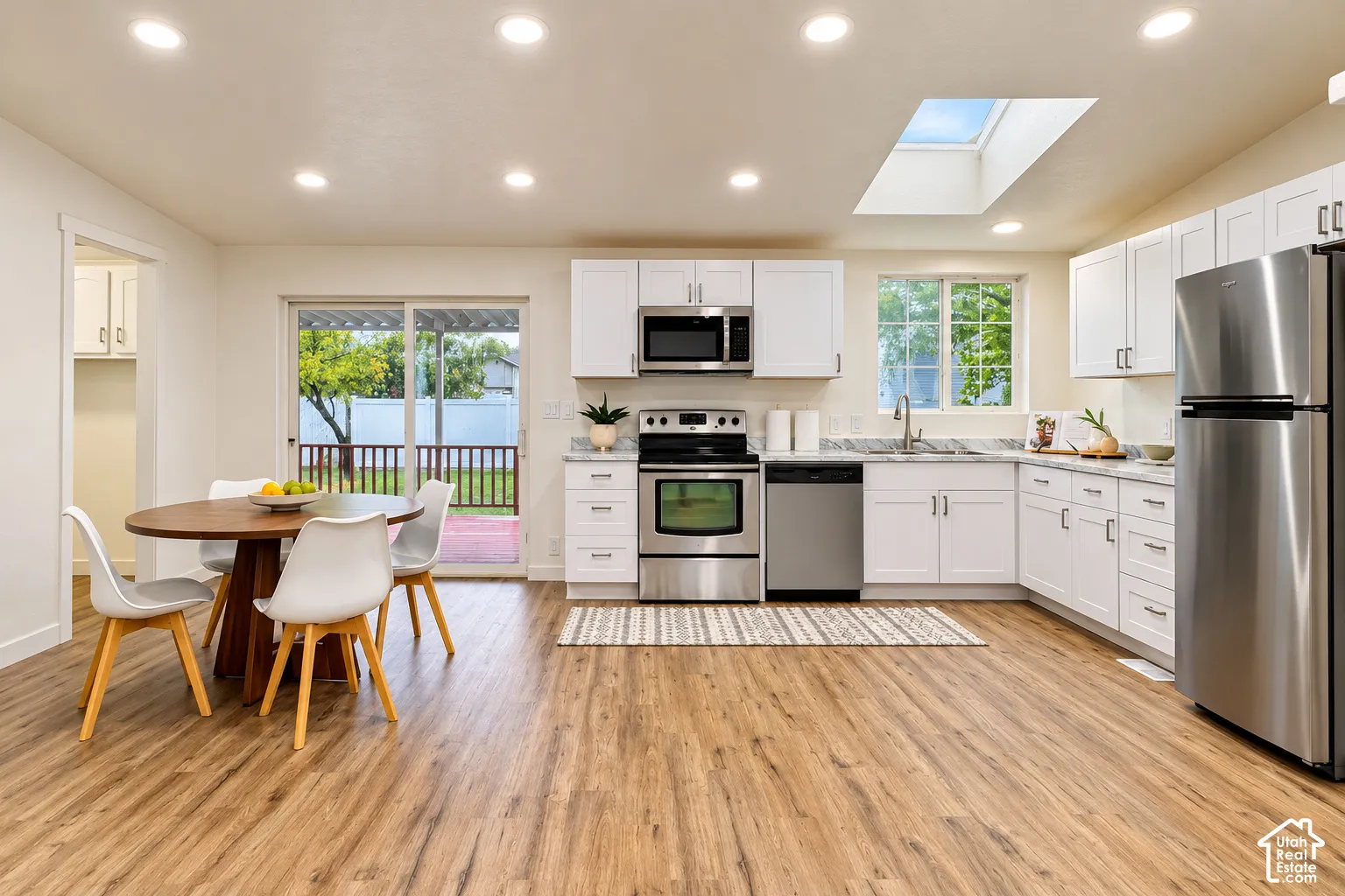 Kitchen featuring white shaker-style cabinetry, stainless steel appliances, wood-finish flooring, a skylight, and recessed lighting