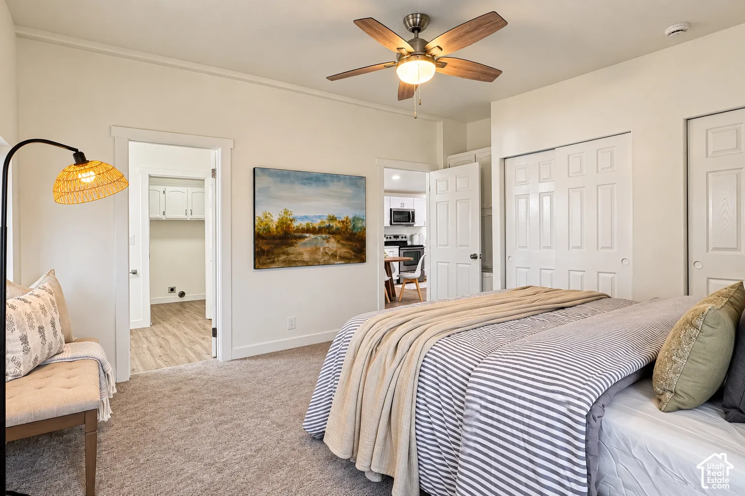 Neutral carpeted flooring, brushed metal ceiling fan with wood-finish blades, sliding closet doors, and multi-panel interior doors