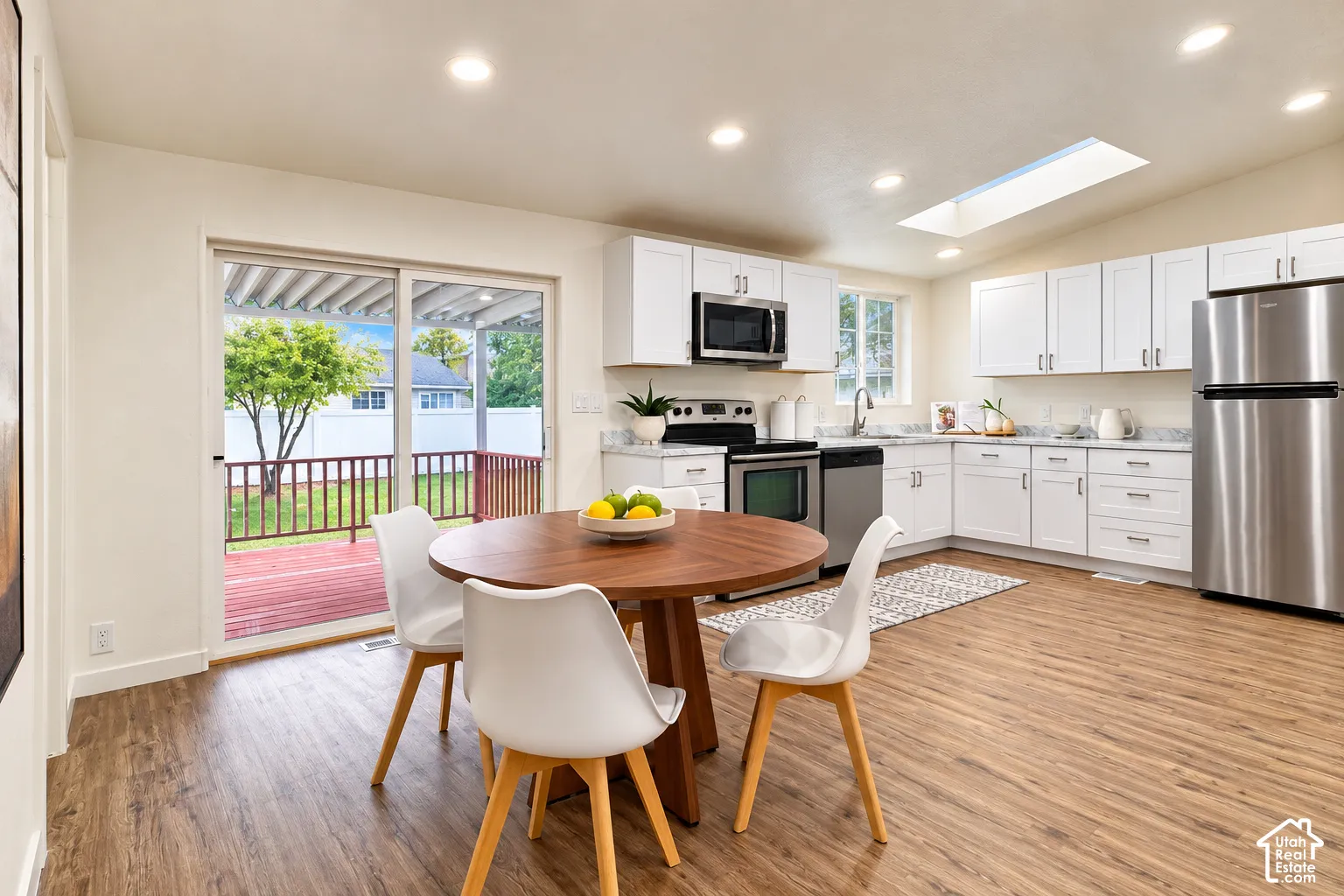 Kitchen featuring white shaker-style cabinetry, stainless steel appliances, wood-finish flooring, a ceiling skylight, and a sliding glass door