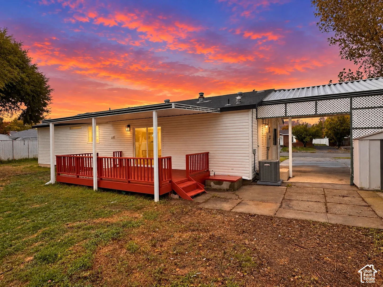 Exterior features include a white siding finish, a covered wooden deck, a paved patio, and a carport with lattice detailing