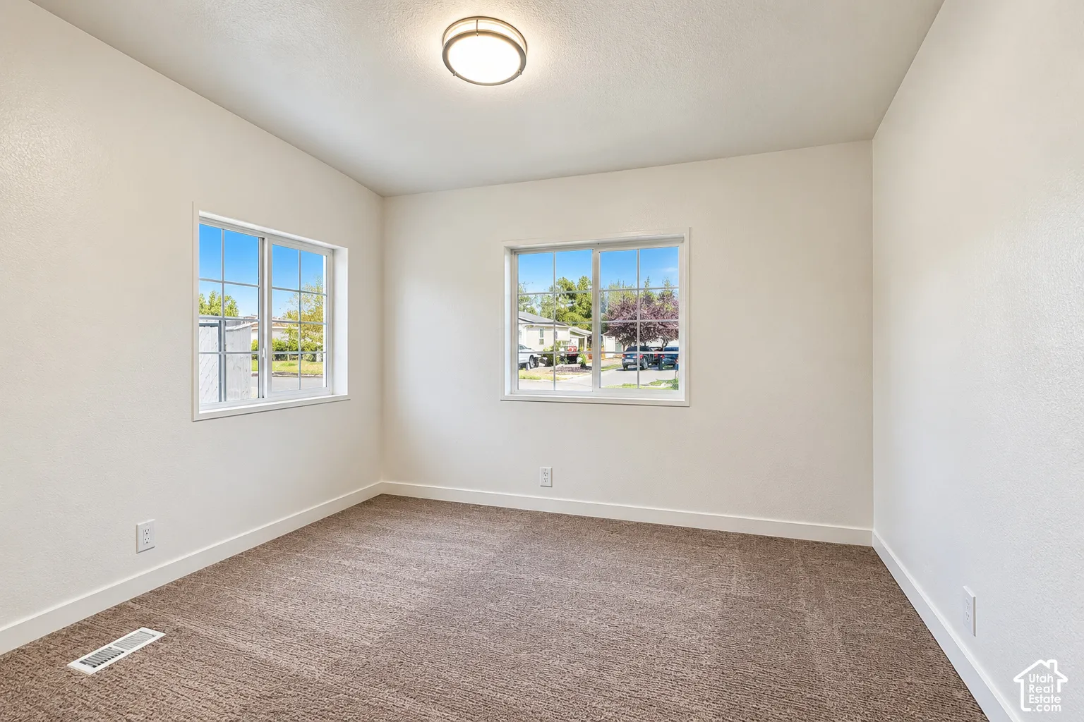 Neutral-toned walls, high-pile carpeting, two dual-pane sliding windows, and a flush-mount circular ceiling light fixture