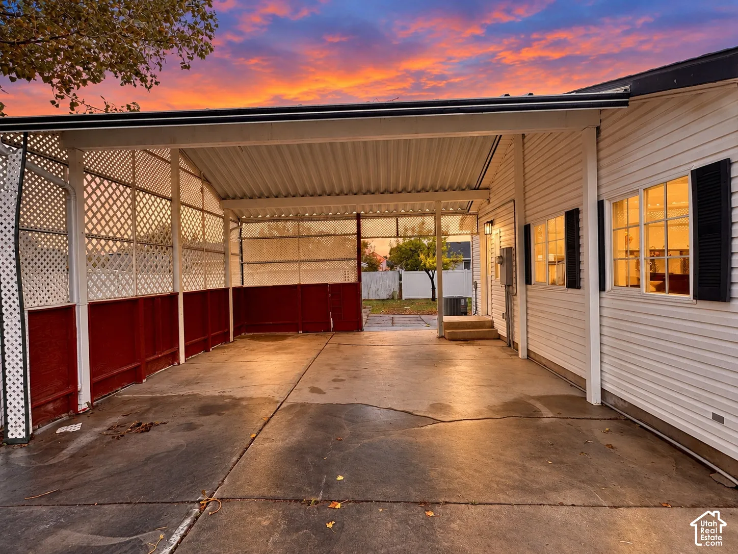 Covered carport with concrete flooring, horizontal lap siding, decorative lattice screen walls, and exterior mounted lighting