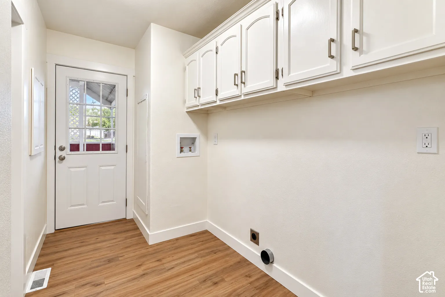 Utility space featuring wood-finish flooring, white upper wall-mounted cabinetry with metal hardware, and an exterior door with a window insert
