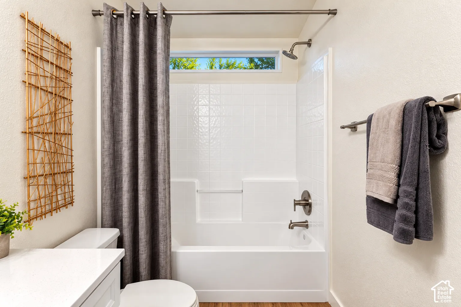 Bathroom featuring a white tub-shower surround with integrated shelving, brushed nickel plumbing fixtures, a transom window, and a white vanity topped with a solid-surface countertop