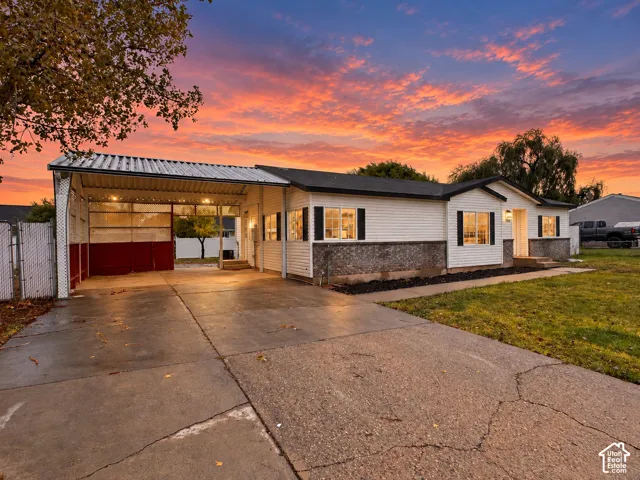 Single-story exterior featuring a metal-roofed carport, stone masonry wainscoting, white horizontal siding, and concrete driveway