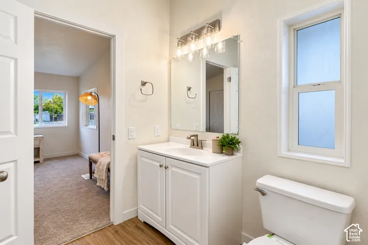 Bathroom featuring a white vanity cabinet with a solid surface countertop, an integrated basin, a three-light fixture, a rectangular wall mirror, and a window with frosted glass