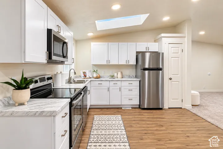 Kitchen featuring white cabinetry, stone-finish countertops, stainless steel appliances, wood-finish flooring, and a ceiling skylight
