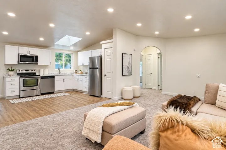 Kitchen featuring white shaker-style cabinetry, stainless steel appliances, wood-finish flooring, a skylight, and an arched doorway