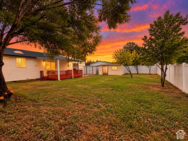 Expansive backyard featuring a wood deck, detached storage structure, privacy fencing, and mature trees
