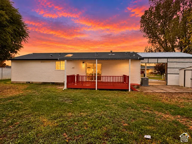 Exterior siding, attached red wood-finish deck, covered carport, and metal storage structure set against a sunset sky