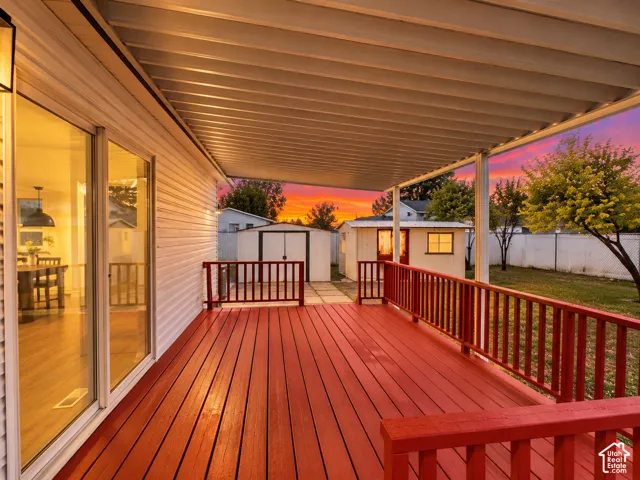 Covered exterior deck with red-painted wood decking and matching railings, sliding glass door, and a detached storage structure