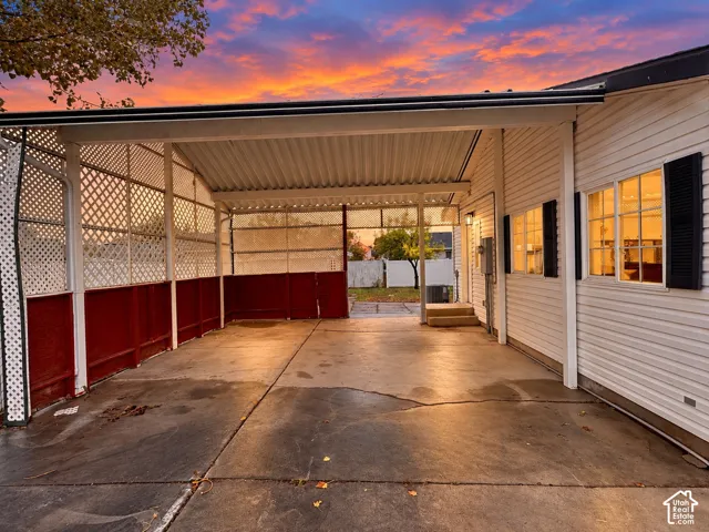 Covered carport with concrete flooring, horizontal lap siding, decorative lattice screen walls, and exterior mounted lighting