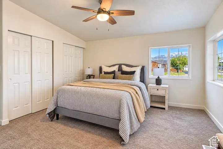 Vaulted ceiling with a five-blade ceiling fan, dual sliding-door closets, neutral wall-to-wall carpeting, and double-pane windows with mountain scenery