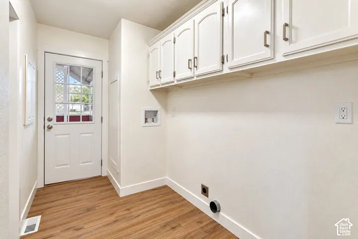 Utility space featuring wood-finish flooring, white upper wall-mounted cabinetry with metal hardware, and an exterior door with a window insert