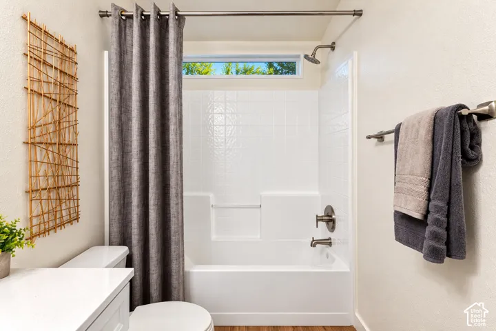 Bathroom featuring a white tub-shower surround with integrated shelving, brushed nickel plumbing fixtures, a transom window, and a white vanity topped with a solid-surface countertop