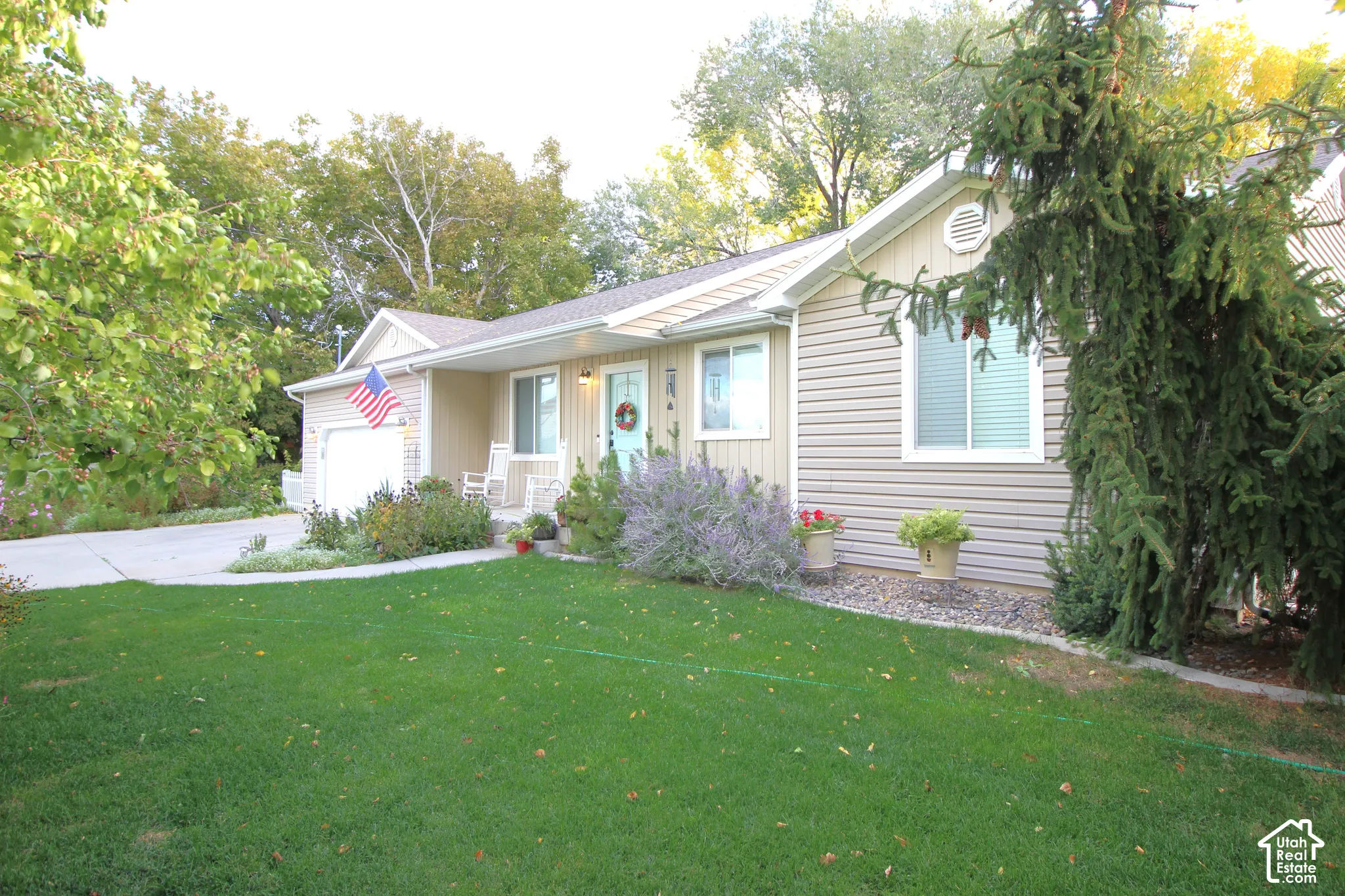 Single-story exterior featuring light-toned horizontal siding, a covered front entryway, concrete driveway, and established landscaping