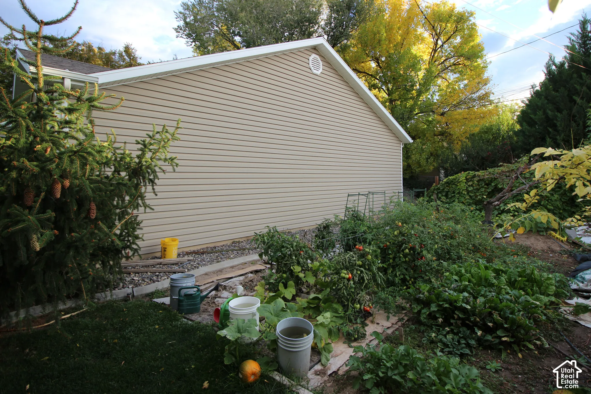 Exterior side elevation featuring horizontal lap siding, gable roofline, and established garden beds