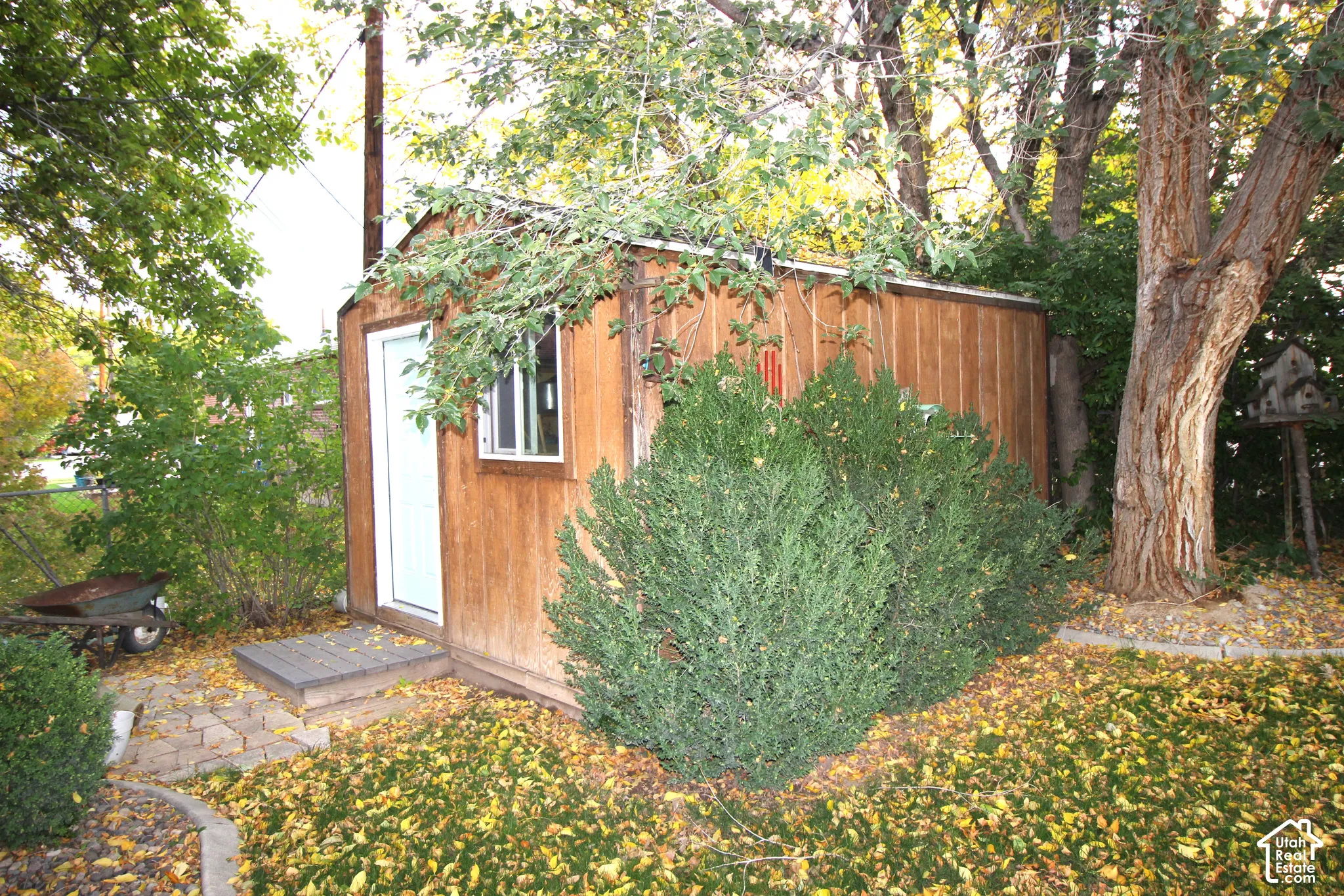 Wood-paneled storage shed featuring a metal-frame window, single-entry door, and paver stone landing