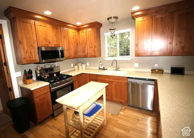 Kitchen featuring warm-tone Knotty Alder wood cabinetry with crown molding, range, dishwasher, solid-surface countertops, wood-finish flooring, and recessed lighting
